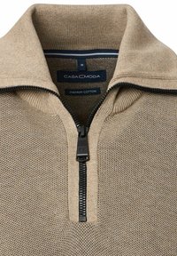 Beżowy rozpinany sweter wykonany z wysokiej jakości bawełny, z teksturowanym wzorem dzianiny, prążkowanym kołnierzem i czarnym zamkiem błyskawicznym. Etykiety są widoczne wewnątrz.