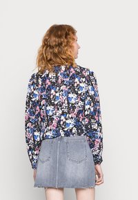 Blusa floral com mangas volumosas em preto, azul, rosa e branco, combinada com uma saia de ganga cinza claro com bainha desfiada e bolsos traseiros.