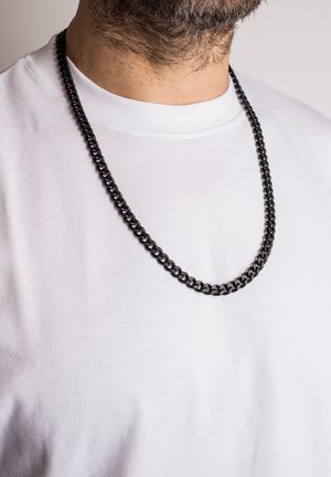 Collana in catena di metallo nero esposta su una maglietta bianca. La catena presenta anelli interconnessi con una superficie liscia e piatta.