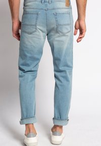 Lyseblå denimjeans med en tapered fit, som har en falmet tekstur, oprullede manchetter og to baglommer. En lys beige logo lap er integreret.