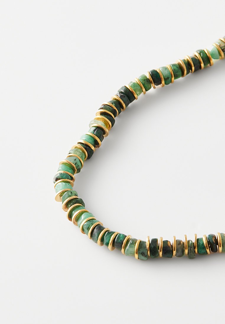 Collier composé de disques en pierre verte séparés par des anneaux dorés. Les pierres affichent différentes nuances de vert avec une texture lisse. Design circulaire.