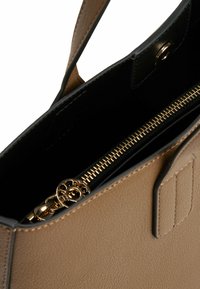 Leren handtas in tan kleur met een zwarte binnenzijde. Bevat een gouden rits en hardware, heeft een gestructureerd ontwerp en een afneembare schouderriem voor veelzijdigheid.