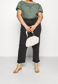 Blusa verde recogida sin hombros, pantalones de mezclilla negros de tiro alto, bolso blanco y sandalias de tiras con tacón bajo.
