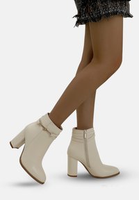 Krämfärgade ankelboots med en slät läderfinish, spetsig tå och en kraftig klack. Inkluderar ett dekorativt band och en siddragkedja.