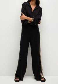 Ensemble de vêtements d'intérieur noir comprenant un haut zippé à col montant et un pantalon à jambes larges. Des bandes latérales en vert, rouge et crème ajoutent du détail.