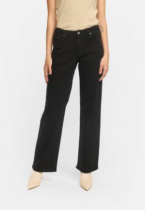 Schwarze weiter Jeans aus Denim mit glatter Textur. Verfügt über fünf Taschen und metallische Beschläge. Kombiniert mit hellen, spitzen Schuhen.