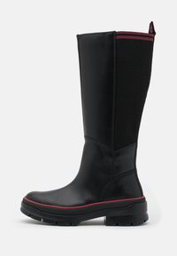 Bottes noires imperméables montantes jusqu'aux genoux avec un avant en cuir lisse et un panneau en tissu côtelé, soulignées par une bordure rouge et une semelle en caoutchouc épaisse.