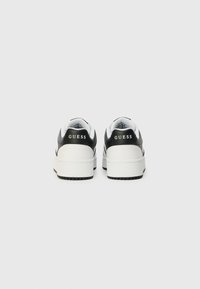 Crno-bijele platforme tenisice s glatkom kožnom završnom obradom, koje imaju podstavljeni ovratnik i "GUESS" logo na peti. Gumeni potplat.