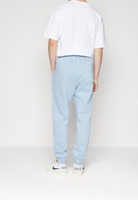 Světle modré tepláky s elastickým pasem, bočními kapsami a ribbenými manžetami, v kombinaci s bílým tričkem s krátkým rukávem a bílými teniskami.