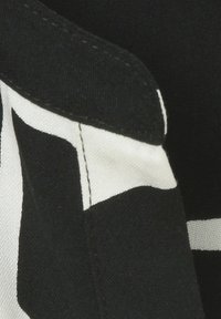 Zwart-wit stof met geometrische patronen en een gladde textuur. Stikdetails zijn zichtbaar langs de randen.