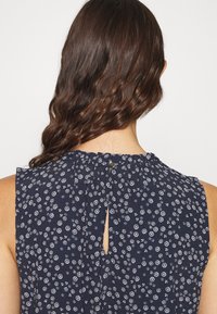 Marinblus med blommönster som har ett nyckelhål i ryggen, är ärmlös och har små vita blommönster över hela. Mjuk, texturerad tyg.