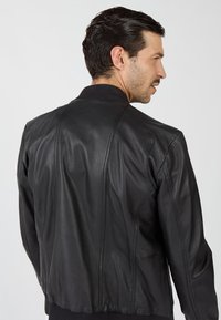 Zwarte leren bomberjack met een geribde kraag en aansluitende manchetten, voorzien van gestikte details en een strakke, op maat gemaakte achterzijde.