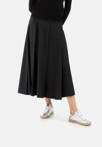 Svart plisserad kjol med ankellång design, tillsammans med silverfärgade metalliska sneakers med texturerad yta och vita snören.