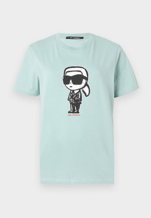T-shirt vert menthe en coton, présentant un motif de dessin animé en noir et blanc d'une silhouette portant des lunettes de soleil et un costume, avec un texte rouge en dessous.