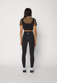 Black mesh crop top with short sleeves, paired with high-waisted black leggings featuring a side logo stripe. Model wears sporty sneakers.