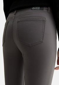Jeans grises ajustados con una textura suave, que cuentan con una etiqueta que dice "Denim Tom Tailor" y dos bolsillos traseros con costuras a medida.