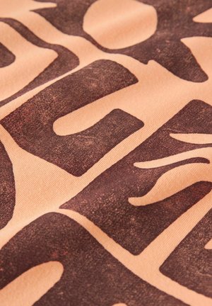 Close-up of faded dark brown block letters printed on light brown fabric, showing textured surface and fabric weave details.