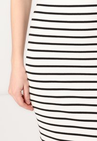 Vestido de malha às riscas preto e branco com um formato justo. Apresenta riscas horizontais, textura suave e uma bainha próxima ao joelho.