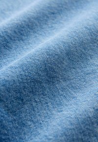 Jasnoniebieska tkanina dżinsowa o charakterystycznym skośnym splocie, ukazująca delikatną fakturę i subtelne zróżnicowania koloru. Gładka powierzchnia bez wzorów.