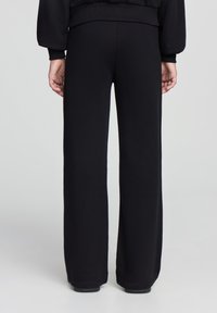 Pantaloni neri a gamba larga realizzati in tessuto morbido. Presentano una vita alta e un design posteriore senza cuciture, offrendo una vestibilità ampia con una silhouette pulita.