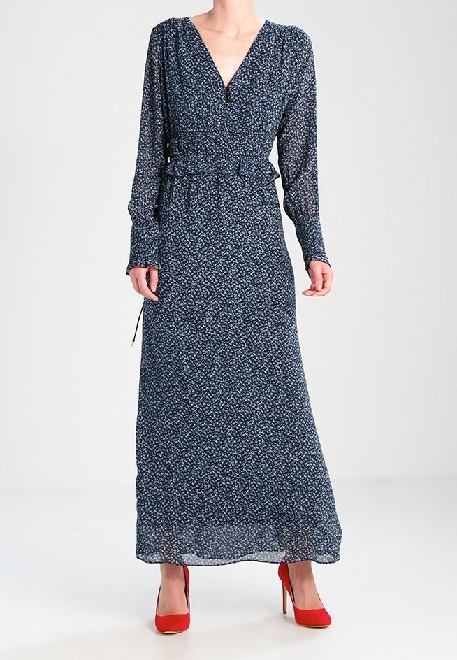 Długa, granatowa sukienka w kwiaty z lekkiego materiału, z głębokim dekoltem w kształcie V i marszczoną talią. Stylizowana z czerwonymi, wysokimi szpilkami, z długimi rękawami.