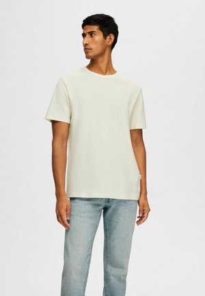 T-shirt corto beige chiaro in cotone morbido, con collo rotondo e vestibilità rilassata. Abbinato a jeans a gamba dritta azzurri.