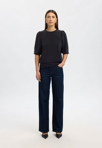 Svart topp med korta ärmar, rund halsringning och puffade ärmar, kombinerad med mörkblå vida jeans och svarta skor med spetsig tå.