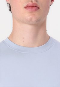 Világoskék, kerek nyakú póló bordázott textúrával, testhez simuló siluettel és finom varrási részletekkel a nyakrészen.