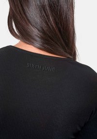 Svart ribbad topp med rundad halsringning och broderad "SIXTH JUNE"-logotyp på baksidan. Slät textur, figurnära design.