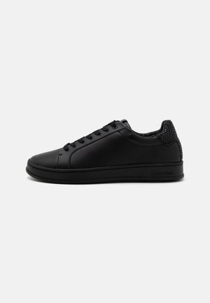 Lage zwarte leren sneaker met veters, gestructureerd hieldetail en platte zool, weergegeven vanaf de binnenkant op een witte achtergrond.