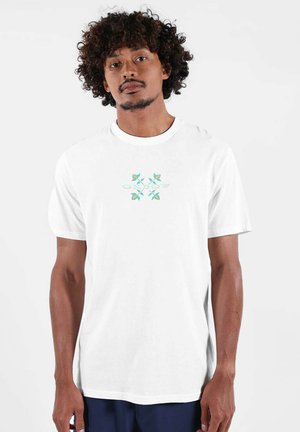 T-shirt en coton blanc avec un motif coloré au centre composé d'éléments floraux verts et bleus, doté d'un col rond et de manches courtes.