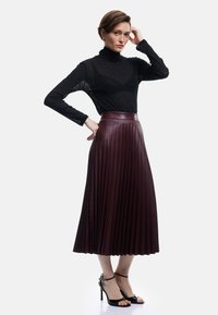Un turtleneck noir à manches longues en maille transparente associé à une jupe en cuir bourgogne plissée arrivant au genou et des sandales à talons aiguilles noires à lanières.