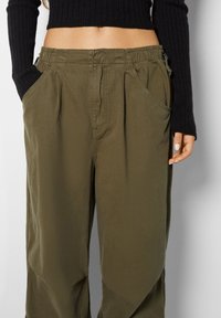 Pantaloni verde oliva realizzati in tessuto leggero, con una vestibilità comoda, vita elastica e tasche frontali con orli inclinati.