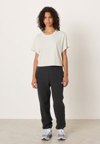 Šviesiai pilka trumpa palaidinė su apvalia iškirpte, derinama su juodomis sportinėmis kelnėmis su elastinga liemene ir balto logotipo detalėmis. Baltos sportbačiai.