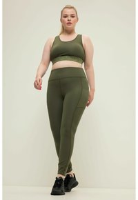 Olijfgroene sportbeha met een getextureerde band, gecombineerd met bijpassende leggings met subtiele stiksels en een hoge tailleband. Zwarte sport schoenen.
