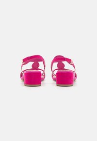 Fuchsia pink heeled sandals feature a soft suede material, a block heel, and ankle straps with a metallic buckle.