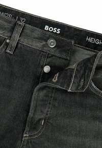 Jeans in denim nero con una texture liscia, hardware in argento, cuciture gialle e un'etichetta con il nome del marchio BOSS.
