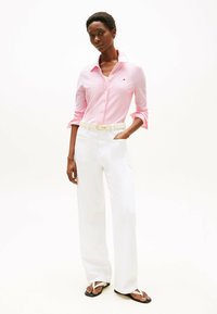 Gestreept roze overhemd met knopen, gecombineerd met hoog uitgesneden witte brede broek en flip-flops, voorzien van een riem en een minimalistisch ontwerp.
