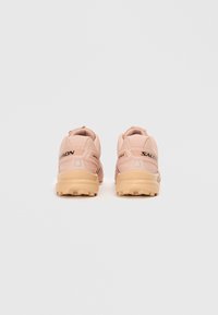 Ténis desportivos rosa com acabamento texturizado, apresentando sola acolchoada, suporte traseiro e detalhe de logótipo da marca em cor escura contrastante.