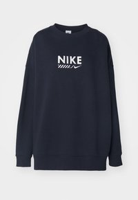 Marint blå sweatshirt tillverkad av bomullsblandning, med en djärv vit "Nike"-logotyp med randiga detaljer över bröstet och ribbade muddar.