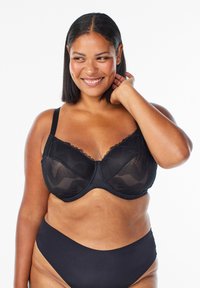 Schwarzer Netz-BH mit floraler Spitze, Unterst&uuml;tzung durch B&uuml;gel, verstellbaren Tr&auml;gern und einer glatten Oberfl&auml;che. Getragen mit passenden schwarzen Panties.