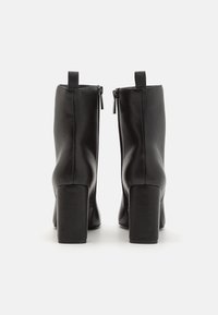 Schwarze Knöchelstiefel aus glattem Leder mit hohem Blockabsatz, ausgestattet mit einem Reißverschluss auf der Rückseite und einem Ziehband für einfaches An- und Ausziehen.