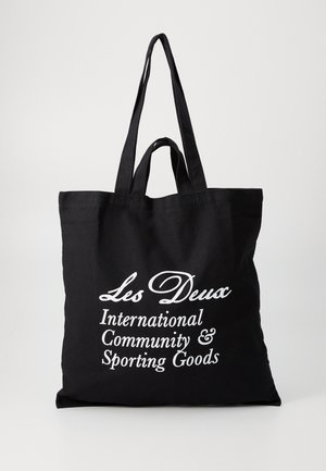 Black canvas tote bag with two sturdy handles, featuring white text: "Les Deux International Community & Sporting Goods."