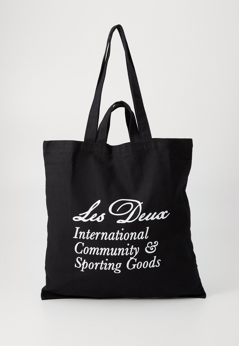 Črna platnena torba z dvema trdnima ročajema, ki vsebuje belo besedilo: "Les Deux International Community & Sporting Goods."