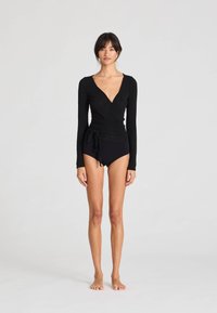 Svart långärmad omlott-body med djup V-ringning och knytdetalj, kombinerad med högmidjade svarta badbyxor. Slät textur.