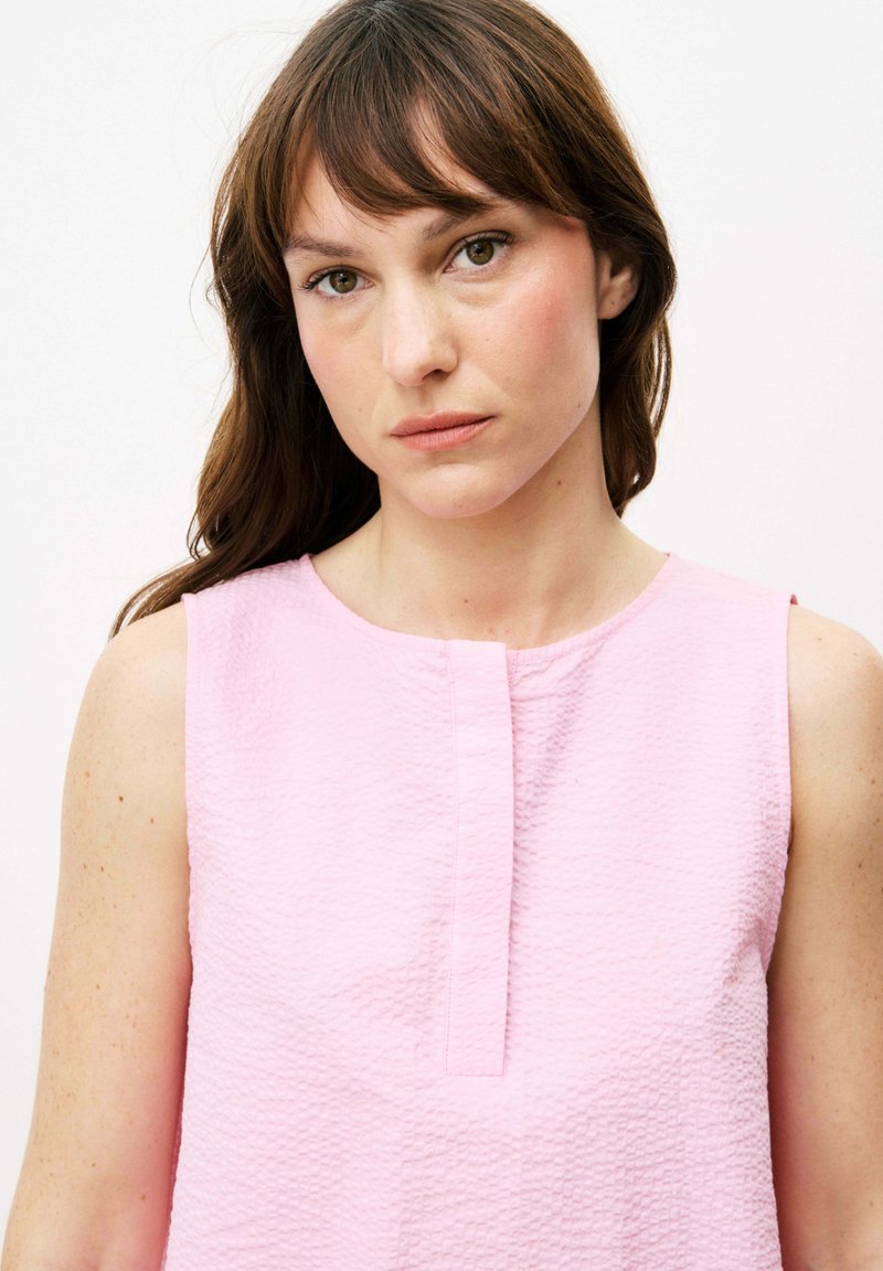 Rosa ärmellose Bluse aus strukturiertem Stoff, mit rundem Ausschnitt und einer Knopfleiste vorne. Das Design weist keine Muster oder Akzente auf.