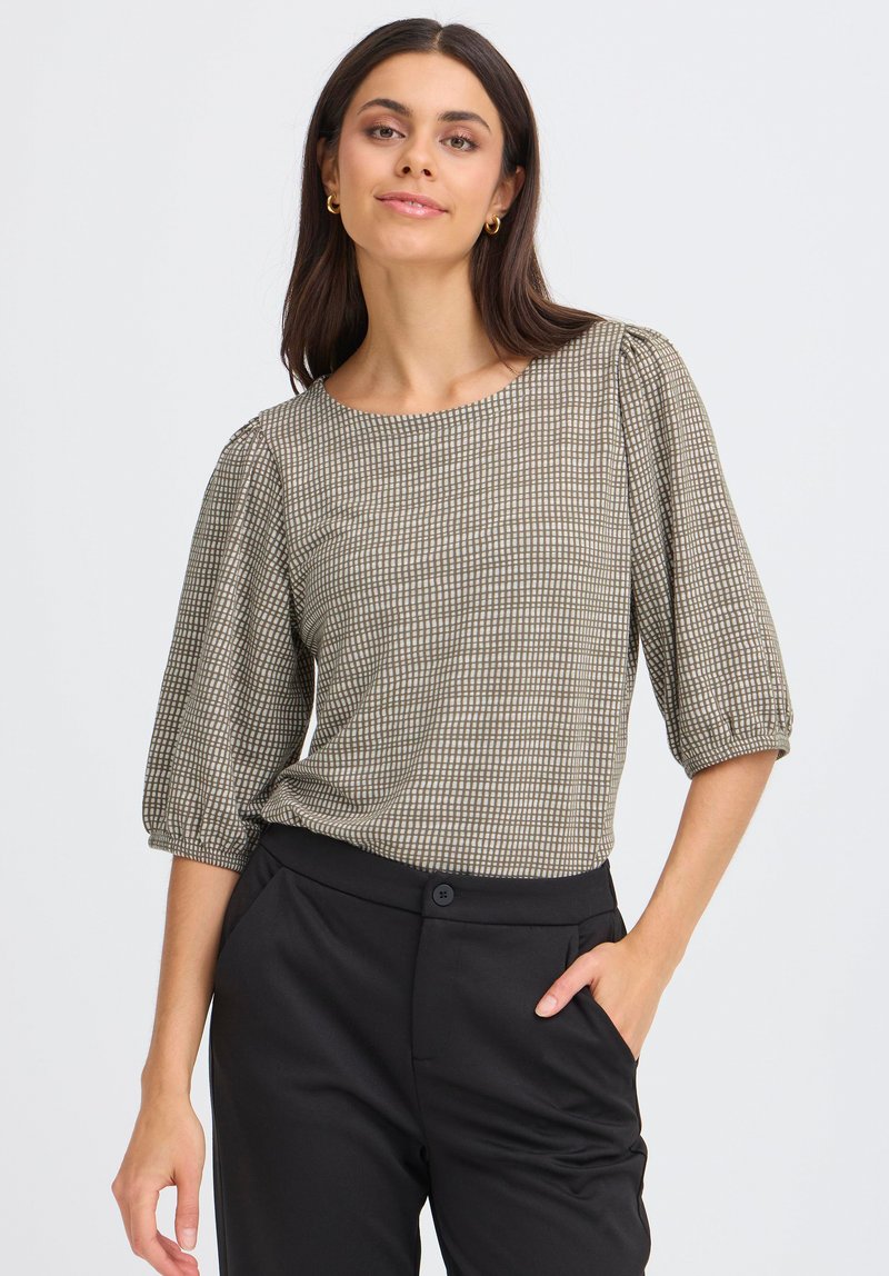 Blouse marron à motifs avec des manches bouffantes et un col rond, assortie à un pantalon noir, présentée contre un fond clair.