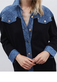 Svart stickad cardigan med en quiltad yoke i jeansstil, silverdetaljer på knapparna och en krage. Har två bröstfickor och långa ärmar.