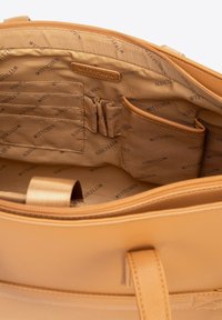 Interior de un bolso de cuero marrón claro que muestra múltiples compartimentos cosidos, ranuras para tarjetas y lazos elásticos en un forro de tela impreso con el texto "WITTCHEN".