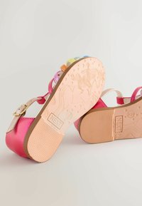 Rózsaszín szandál csillogó felülettel, több színben pompázó pántokkal és texturált rózsaszín gumitalppal, melyen unikornis minta és márkajelzés látható.
